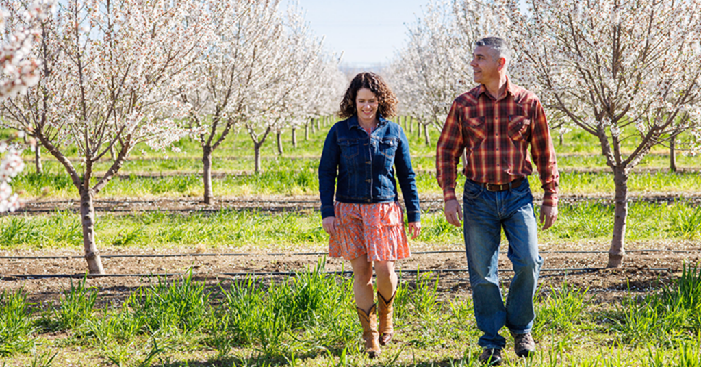 Woman and man walking in an almond orchard on a sunny day.
