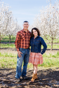 Man and woman smiling and standing together in a blooming almond orchard.