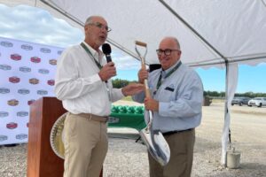 Man holding mic and another man holding a shovel during a facility opening.