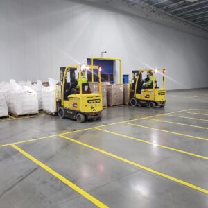 Two yellow forklifts loading pallets of boxes inside a warehouse.