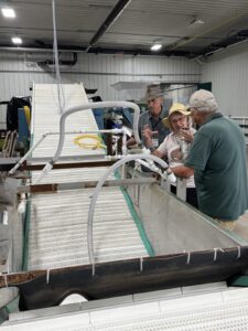 Men and women standing near nut processing equipment in a warehouse.
