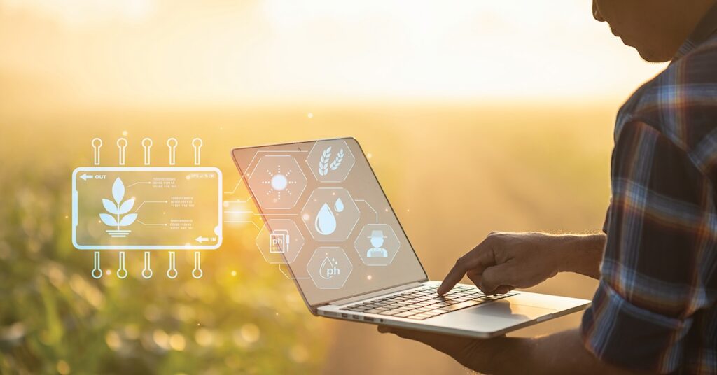 Farmer holding laptop with tech symbols on the screen.