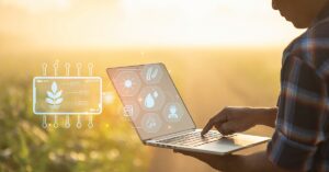 Farmer holding laptop with tech symbols on the screen.