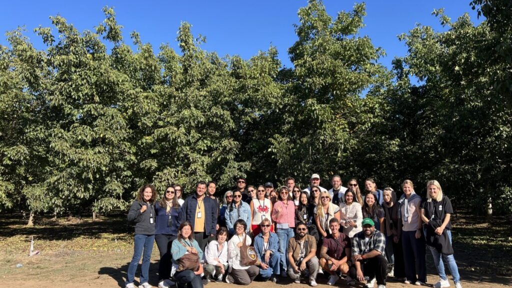 Group of men and women posing for a group shot in a walnut orchard.
