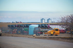 An assortment of large farm equipment parked in the foreground, with silos in the background.