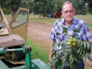 Buddy Leger standing next to a piece of farm equipment while holding a pecan branch.