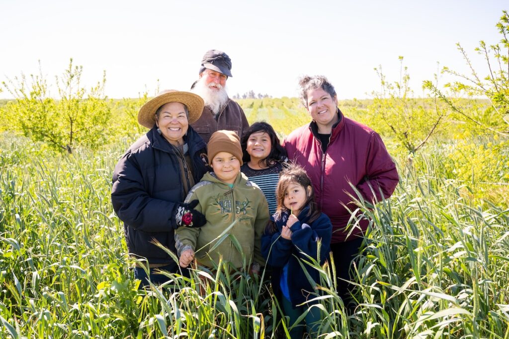 Multi-generational family of smiling farmers standing in a field.