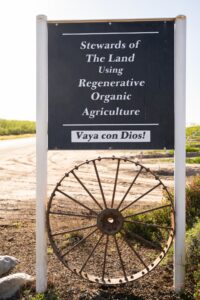 Sign that reads "Stewards of The Land Using Regenerative Organic Agriculture. Vaya con Dios!"
