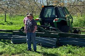 Two farm workers standing in front of a piece of farm equipment.