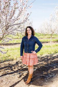 woman standing in an orchard posing with left hand on left hip