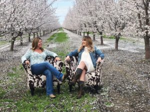 two women sitting in cow print chair in an orchard of flowering trees